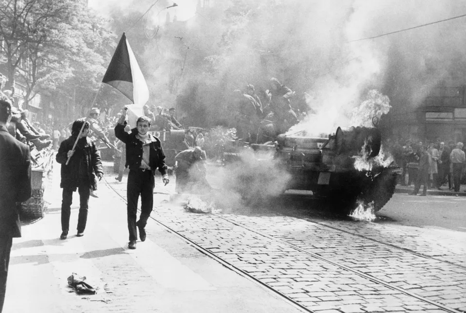 불타는 전차 옆으로 국기를 들고 지나가는 프라하 시민들 — 1968년 8월 소련군 침공 때